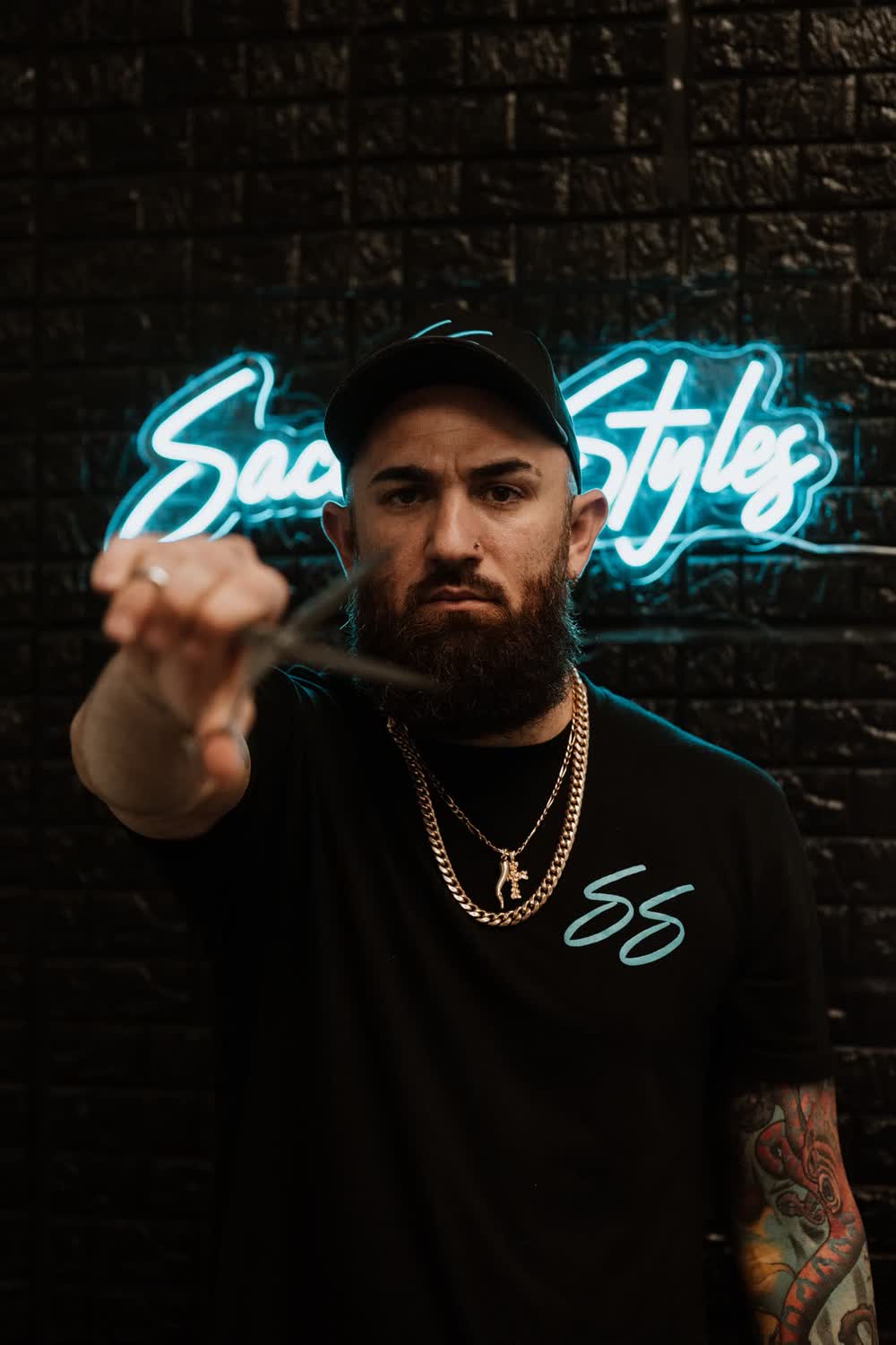 Barber Chris Sacconi holding his scissors in front of the glowing Sacconi Styles sign